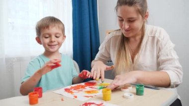 Kirli elleri boyalı, gülümseyen mutlu bir çocuk. Annesinin parmakları ve bıyıklarıyla çizdiği resme bakıyor. Aile birlikte eğleniyor ve resim çiziyor..