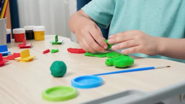 Nahaufnahme eines kleinen Jungen, der mit Händen bunte Knetmasse oder Ton formt und formt. Spezieller bunter Teig zur Förderung der Motorik der Kinder. Kindererziehung, Kreativität und Kunst. — Stockvideo