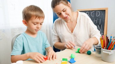 Gülümseyen anne oğluna renkli kil ya da plastikle şekil yapmayı öğretiyor. Aile şekillendirmek için oyuncak hamuruyla oynuyor