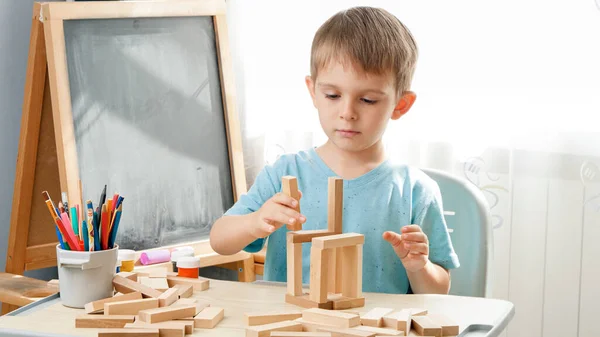 Porträtt av en liten pojke som leker med leksaksblock av trä och byggtorn från tegel. Begreppet smarta barn och hemundervisning under inlåsning och självisolering — Stockfoto