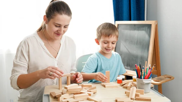 Mały chłopczyk z matką budującą wieżę z drewnianych bloków. Koncepcja inteligentnych dzieci i wychowania domowego podczas zamykania i samoizolacji. Rodzicielstwo i nauczanie dzieci. — Zdjęcie stockowe