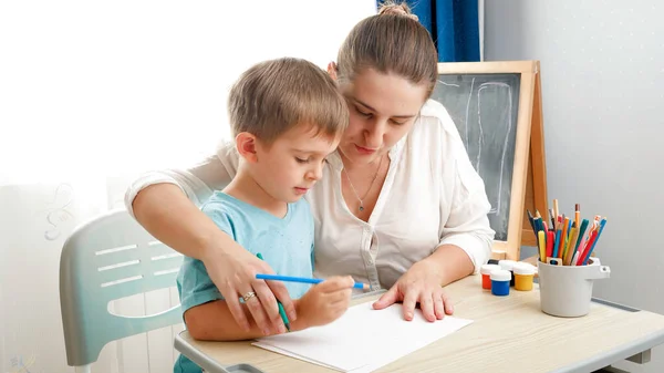 Мама учит рисованию и пишет своему маленькому сыну. Мальчик учится писать карандашом на дому Концепция образования и дистанционной школы дома во время изоляции и самоизоляции. — стоковое фото
