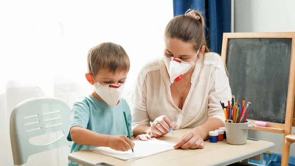 Giovane insegnante di sesso femminile e bambino con indosso respiratori maschera protettiva che studiano in classe. Genitori che proteggono i bambini dal virus durante l'isolamento e l'autoisolamento. Scuola remota e — Foto Stock