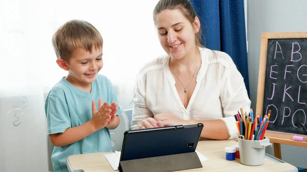 Sonriente niño feliz estudiando y aprendiendo en la tableta con la joven madre sonriente. Educación en el hogar y la escuela remota, Hacer los deberes en la computadora tableta —  Fotos de Stock