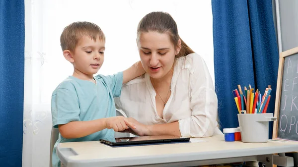 Niño feliz con la madre jugando en la tableta después de estudiar y aprender en casa. Tablet PC digital y gadgets en la educación. Escuela remota durante el bloqueo —  Fotos de Stock