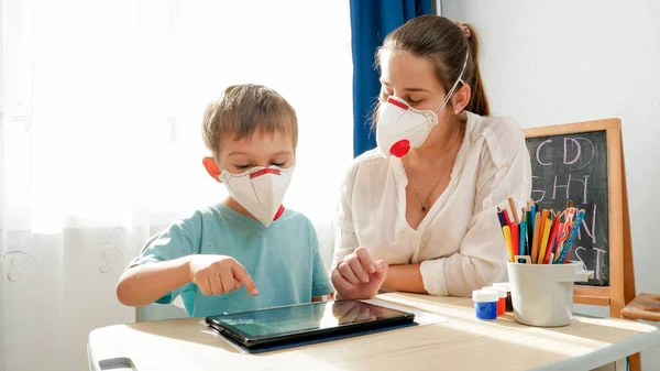 Petit garçon portant un masque médical protecteur respirateur étudiant en classe avec une enseignante. Faire des devoirs et étudier à la maison avec les parents pendant le confinement et l'auto-isolement. — Photo