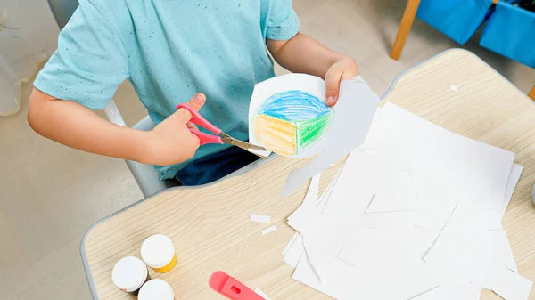 Primer plano del niño inteligente recortando dibujo dibujado con tijeras. Niños estudiando y aprendiendo detrás del escritorio escolar en casa — Foto de Stock