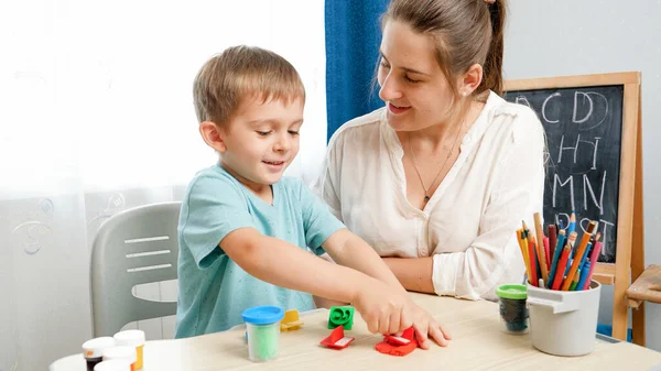 Feliz niño sonriente jugando con sellos y arcilla colorida con la madre. Niño usando arcilla y jugando masa — Foto de Stock