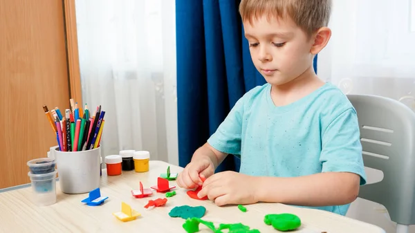 Leende barn pojke forma och skulptera former och former med färgglada deg eller plasticine. Användning av leksakslera i utbildning och lärande i hemmet — Stockfoto