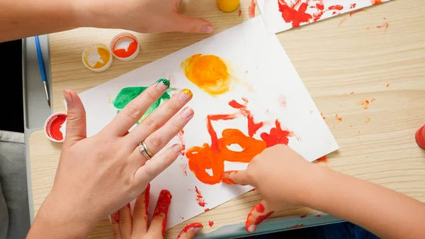 Vista superior de niño pequeño con dibujo de la madre y la pintura con las manos cubiertas de pintura de colores sobre papel blanco. Concepto de educación infantil, desarrollo creativo y arte. — Foto de Stock