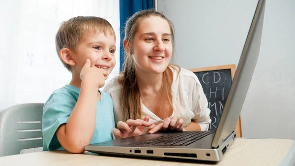 Szczęśliwy chłopczyk z uśmiechniętą matką i patrzący na ekran laptopa. Niesamowite dziecko korzystające z laptopa — Zdjęcie stockowe