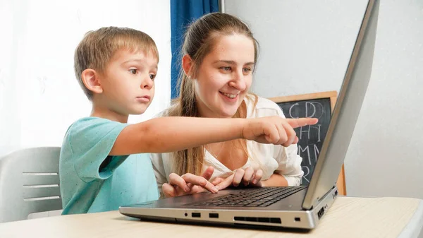 Menino incrível apontando com o dedo na tela do laptop. Criança incrível mostrando emoções positivas ao usar o computador portátil — Fotografia de Stock