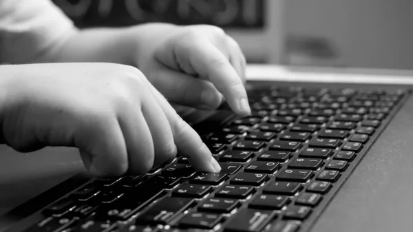 Black and white closeup photo of child pressig buttons on computer keyboard, typing message on laptop keyboard. — Stock Photo, Image