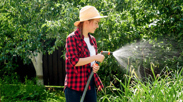 Портрет улыбающейся девушки с водяным шлангом, поливающей овощи на заднем дворе сада. Выращивание и уход за органическими овощами в саду