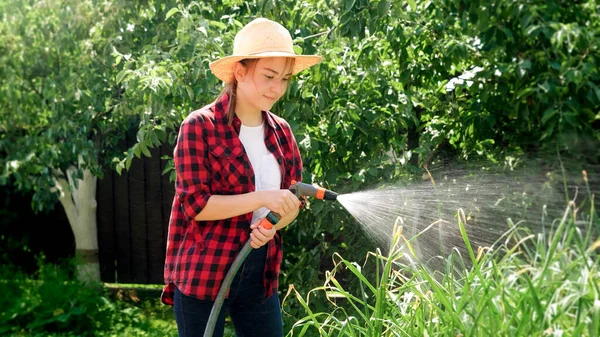 Giovane donna in cappello contadino irrigazione verdure biologiche verdi che crescono a frutteto. Persone che lavorano nel giardino e nel frutteto — Foto Stock