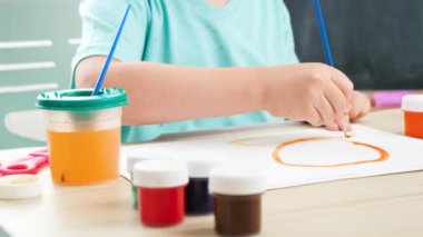 Küçük çocuğun, fırça kullanarak renkli boyayla resim çizdiği yakın plan. Tecrit ve tecrit süresince evde çocuk eğitimi. Sanat kavramı ve çocukların yaratıcılığı