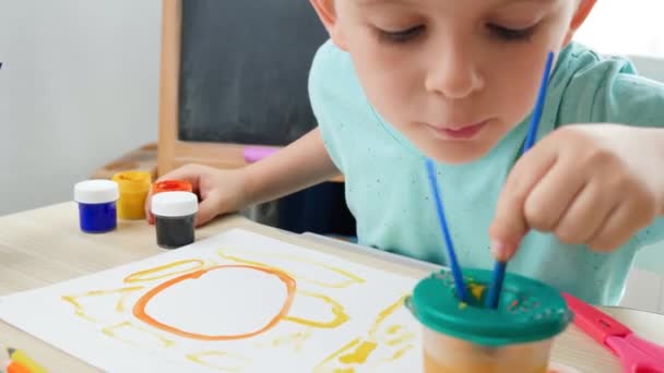 可爱男孩用彩绘画笔把画笔浇注在彩绘的画布上,画出美丽的图画.有创意的孩子在画艺术。封锁期间的家庭教育 — 图库视频影像