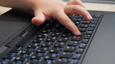 Laptop klavyesindeki küçük çocuk eli ve parmak tuşlarının yakın çekim videosu. Bilgisayar klavyesine kelime yazan çocuk.