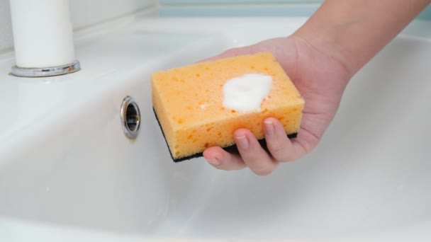 Zbliżenie stosowania środków czyszczących lub detergentów na żółtą gąbkę i czyszczenie zlewu z białą wodą w łazience. Koncepcja higieny i ciężkich prac domowych kobiet. — Wideo stockowe