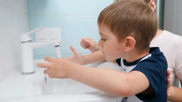 Медленное движение маленького мальчика, моющего рот и лицо водой из крана в ванной комнате. Концепция детской гигиены и здравоохранения. — стоковое видео