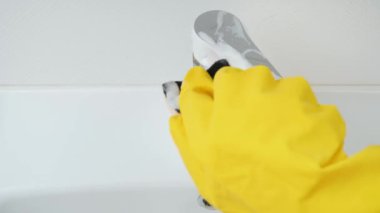 Ruber eldivenli bir kadının banyo lavabosundaki parlak su musluğunu yıkaması ve temizlemesi.