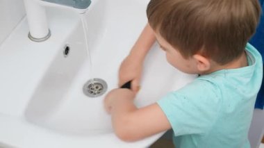 Su lavabosunu ovalayan ya da lavaboyu sünger ve kimyasal deterjanla ovalayan küçük çocuğun en iyi görüntüsü. çocuk, ebeveynlerin evi temizlemesine yardım ediyor