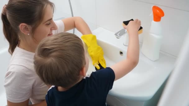 Gülümseyen küçük çocuk evde annesinin banyo yıkamasına ve temizlemesine yardım ediyor. Çocuk ve yetişkin ev işi yapıyor — Stok video