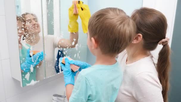 Щаслива усміхнена мати з маленьким сином робить прибирання будинку та миття дзеркала у ванній кімнаті. Сім'я посміхається і проводить час разом, роблячи домашнє завдання — стокове відео
