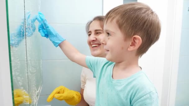 Lycklig mor med liten son rita på smutsig spegel medan du gör housecleanup och hushållsarbete. Familjen har trevligt tillsammans. — Stockvideo