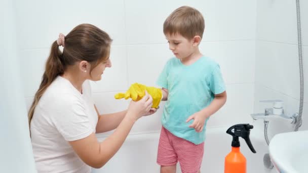 Маленький маленький хлопчик носить і одягає захисні гумові рукавички перед чищенням та миттям у ванній кімнаті . — стокове відео