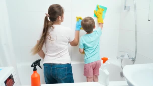 Pequeño niño con madre joven lavando y limpiando paredes de azulejos en el baño mientras hace tareas domésticas y limpieza en el hogar — Vídeos de Stock