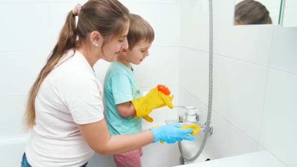 お風呂と水のシンクを洗う母親と笑顔の男の子。家事や家庭清掃で大人を助ける子供たち. — ストック動画