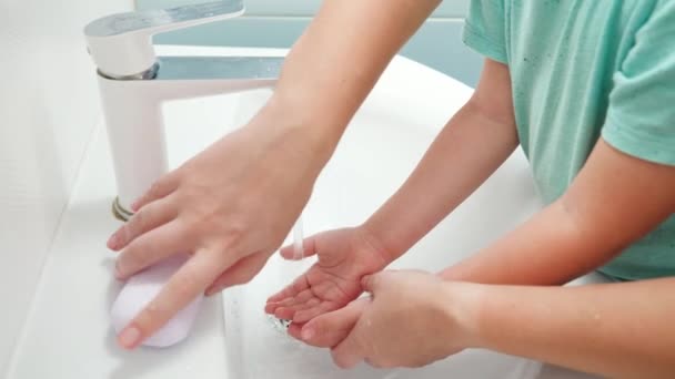 CLoseup van moeder die les geeft en haar zoontje laat zien hoe ze handen moet wassen. Kind met behulp van antibacteriële zeep tijdens het wassen van de handen in de badkamer — Stockvideo