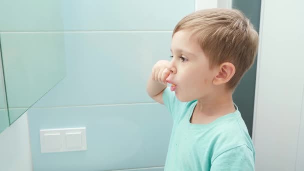 Retrato do menino criança olhando no espelho enquanto escova os dentes de manhã. Higiene infantil e cuidados de saúde — Vídeo de Stock