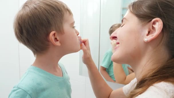 Jovem mãe carinhosa escovando e limpando os dentes de seu pequeno filho. Pais e crianças cuidando da saúde e higiene dos dentes — Vídeo de Stock