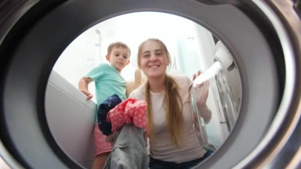 Leende småbarn pojke med mamma lasta kläder och leksaker i tvättmaskin. Familjen har roligt i hushållsarbete och daglig rutin — Stockvideo