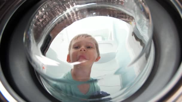 Смішний усміхнений маленький хлопчик дивиться всередину барабана пральної машини — стокове відео