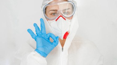 Sağlık çalışanı ya da doktor portresi takım elbise ve maskeyle korunurken parmaklarıyla onay işareti gösteriyor. Küresel salgın ve tecrit