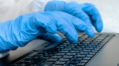 Laptopta çalışan koruyucu lastik eldivenli doktorlara yakın çekim. Tıbbi eldivenlerle klavye yazma ve kullanma