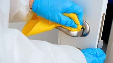 Koruyucu sağlık giysisi giyen, eldivenli, temizlik yapan ve kapı kollarını yıkayan kadınlara yakın çekim. İnsanlar covid-19 ve coronavirüs 'e karşı mücadele ediyor.