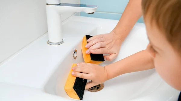 Primer plano del niño ayudando a la madre lavabo con esponja y detergente en el baño. COncept de trabajo en equipo familiar y trabajo doméstico — Foto de Stock