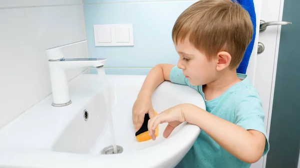 小さな幼児の男の子は家事をしながらバスルームで水を洗うと両親を助ける — ストック写真