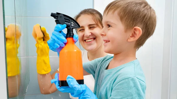 Malý batole chlapec nanášení chemického čisticího prostředku ze spreje při mytí koupelnového zrcadla s matkou. Děti a dospělí dělají domácí práce a úklid doma — Stock fotografie
