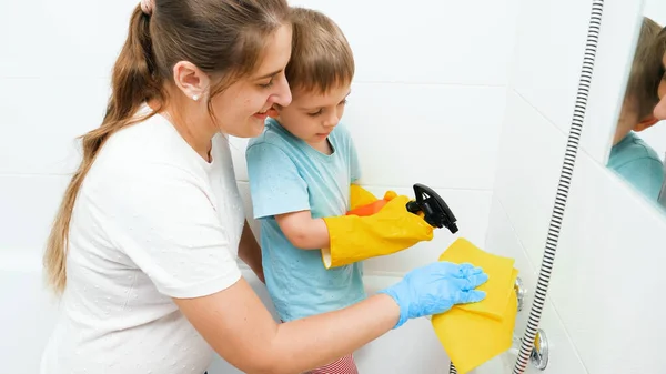 お母さんの洗濯や掃除用の水で小さな幼児の男の子はバスルームでタップします。掃除や家事をする幸せな笑顔の家族 — ストック写真