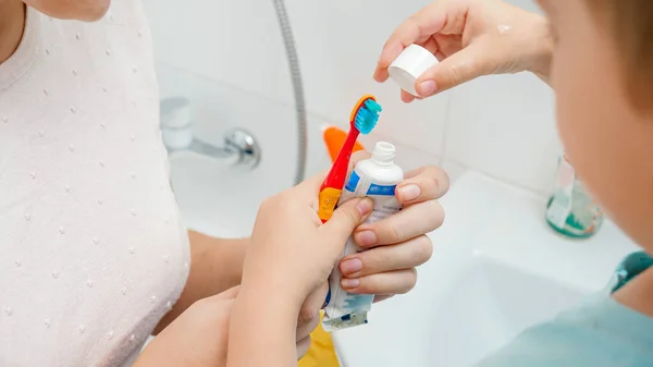 Primer plano de la madre ayudando a su hijo pequeño a aplicar pasta dental. Niño usando cepillo de dientes y pasta de dientes para cepillarse y limpiar los dientes — Foto de Stock