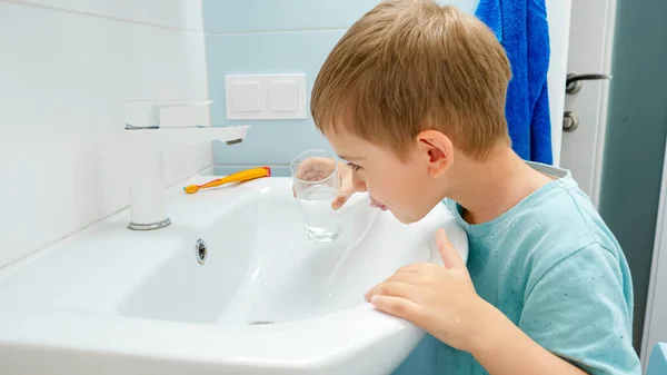 Retrato de niño sonriente enjuagando la boca con agua de vidrio después de cepillarse y limpiar los dientes con cepillo de dientes y pasta de dientes. Concepto de higiene dental y rutina diaria — Foto de Stock