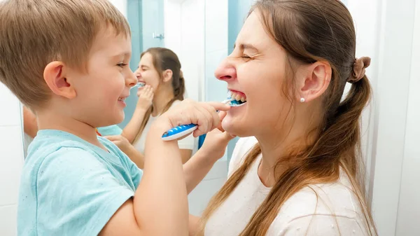 Divertido niño pequeño limpiando y cepillando los dientes de las madres. Concepto de higiene familiar y cuidado de los dientes — Foto de Stock