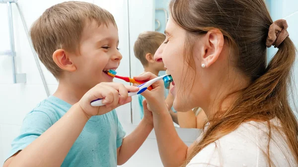 Niño sonriente con madre joven cepillándose los dientes y limpiándose la boca con cepillos de dientes. Familia divirtiéndose mientras cuida los dientes higiene y atención médica — Foto de Stock
