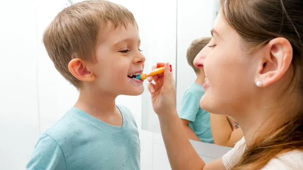 Joven madre cuidadora cepillando y limpiando los dientes de su pequeño hijo. Padres e hijos cuidando los dientes salud e higiene — Foto de Stock