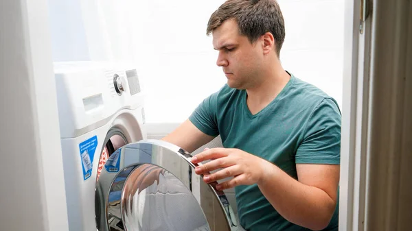 Ung stilig man lastar smutsiga kläder i tvättmaskin och tvättar. Manligt hushållsarbete och daglig rutin hemma — Stockfoto